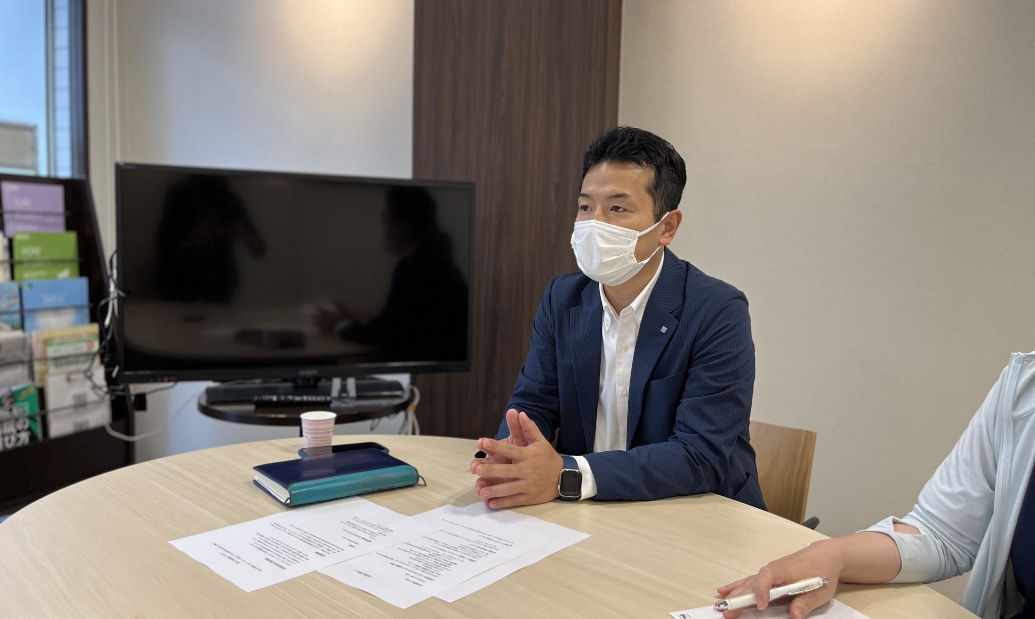 会議室でマスクを着用して打ち合わせをするスーツ姿の男性と他の出席者