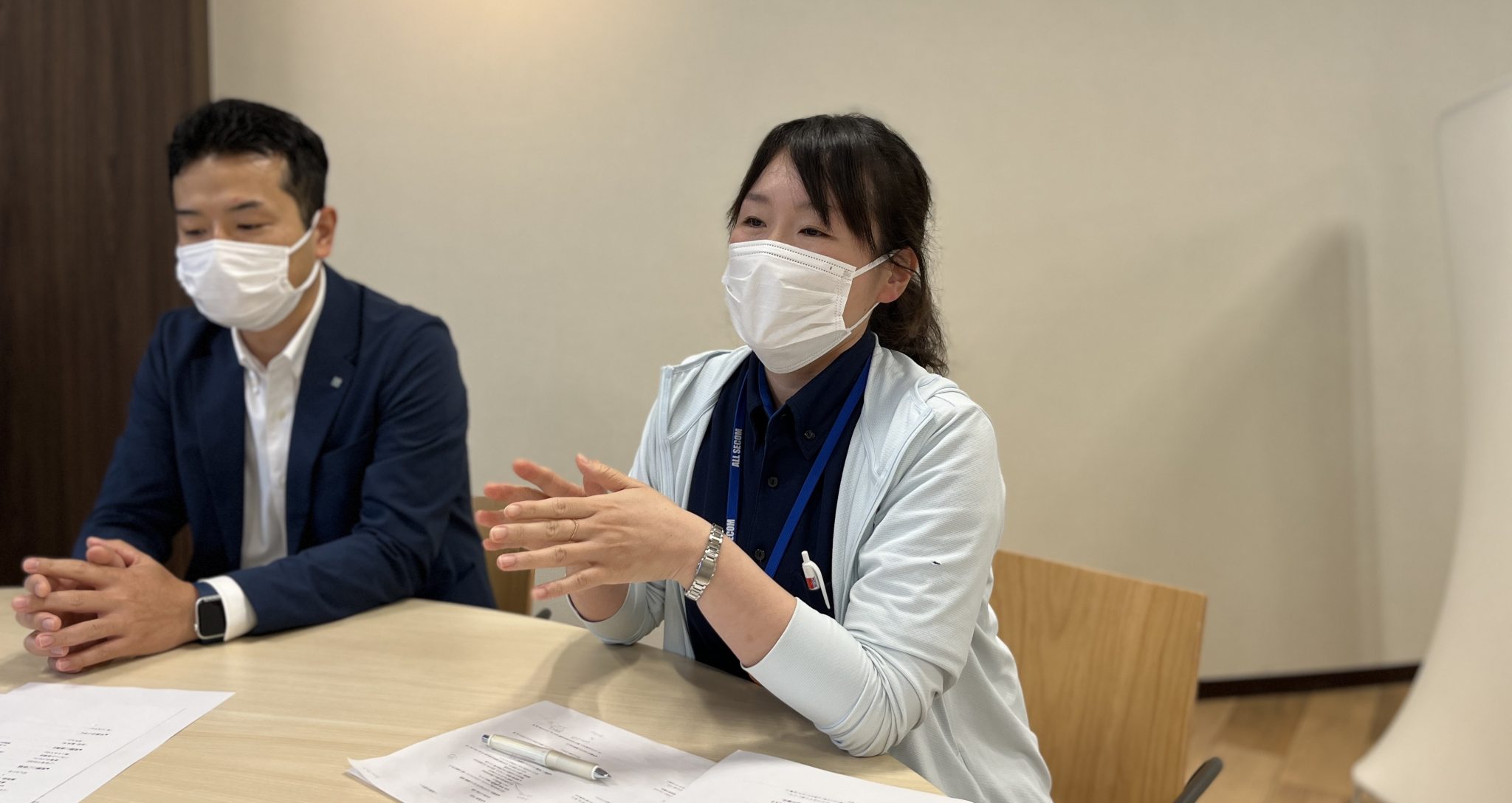 マスクを着用し、会議中に説明をする女性と、それを見守る男性の様子