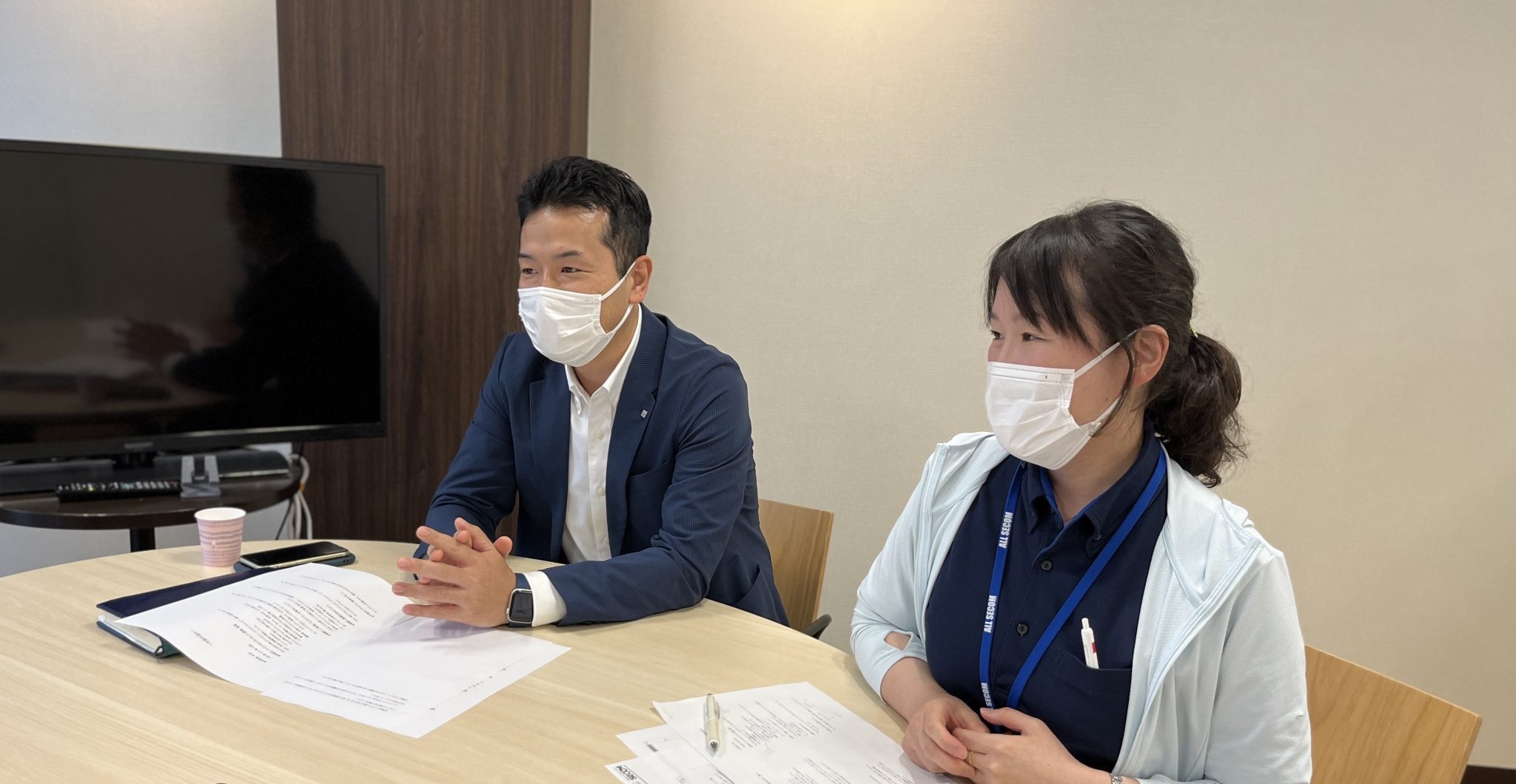 マスクを着用し、会議中に説明をする女性と、それを見守る男性の様子