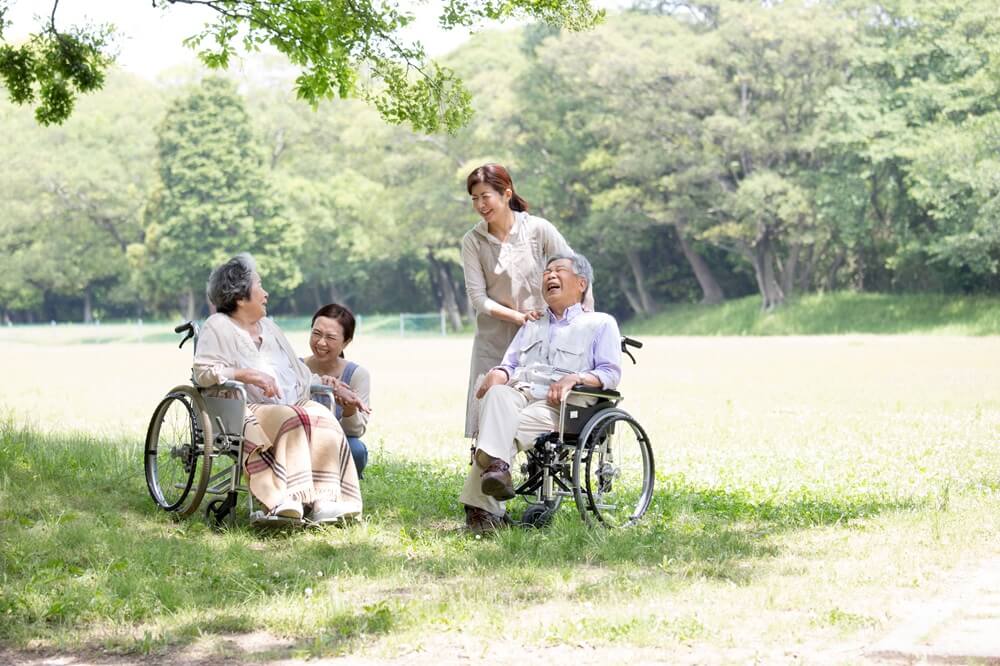 介護士と車椅子の高齢者が公園でリラックスして談笑する様子