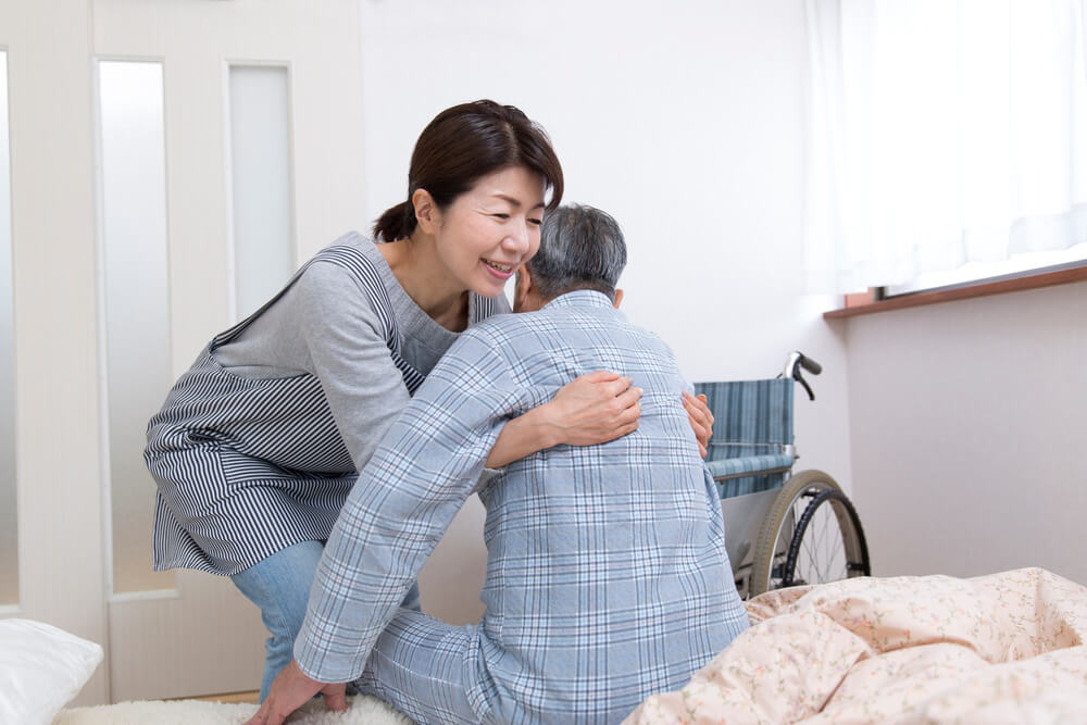 高齢者を笑顔で支える家族介護者と車いすのある居室の様子