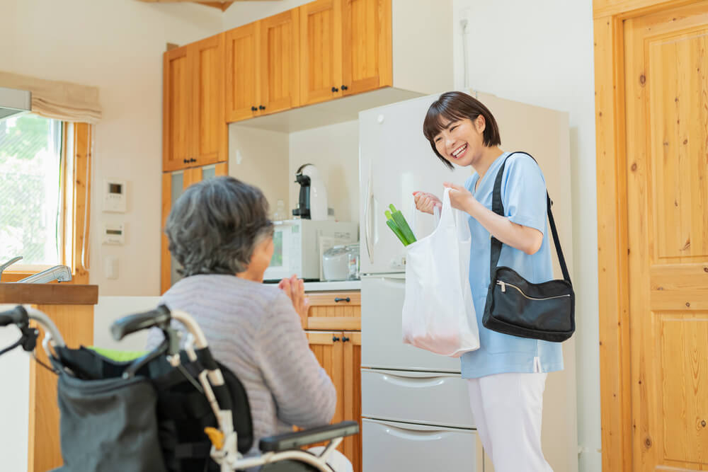 看護師が買い物から帰ってきて、車椅子に乗っている高齢者と会話している様子